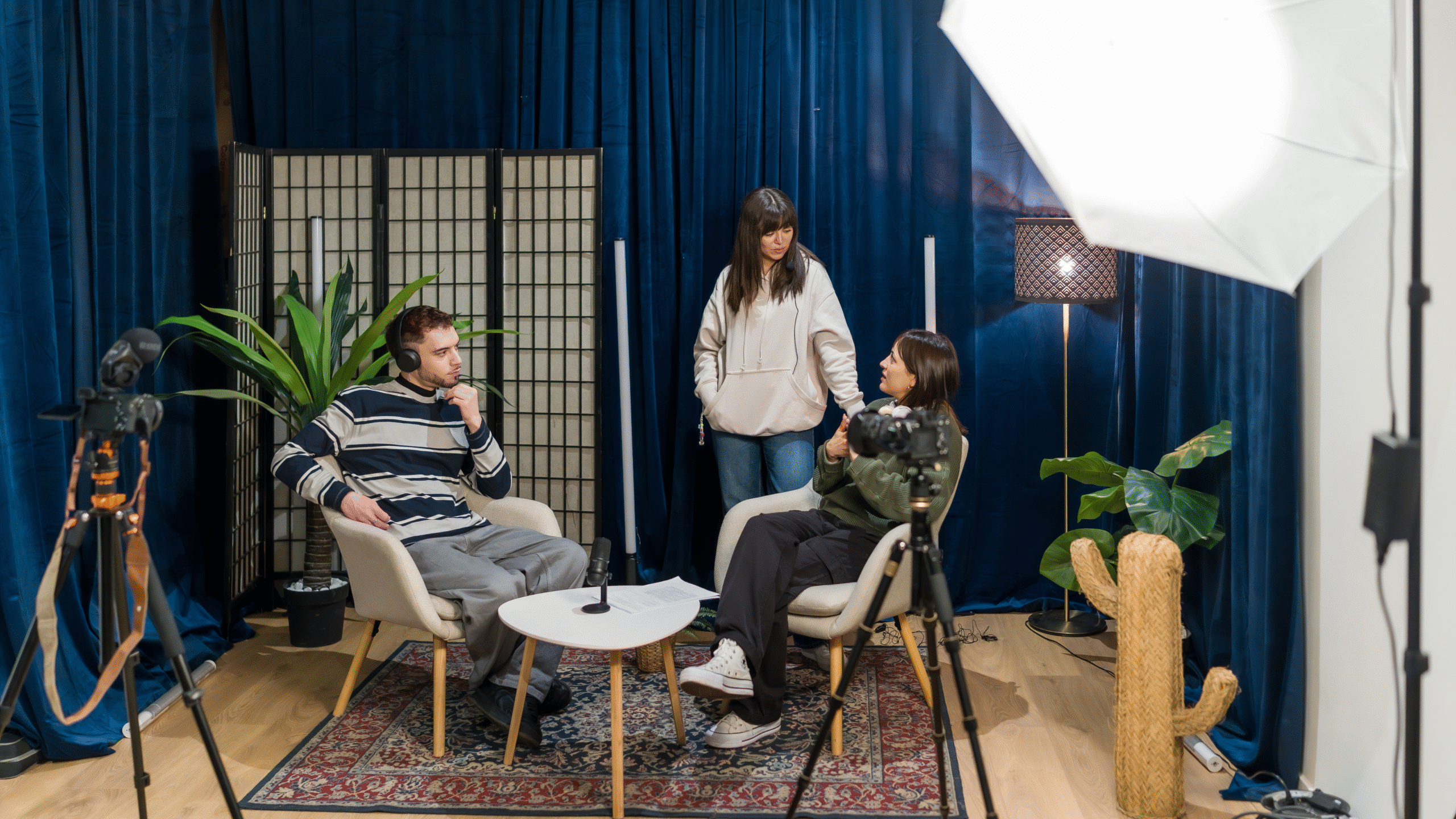 Media production studio with podcast recording setup, cameras, lighting equipment, and content creators filming digital media content