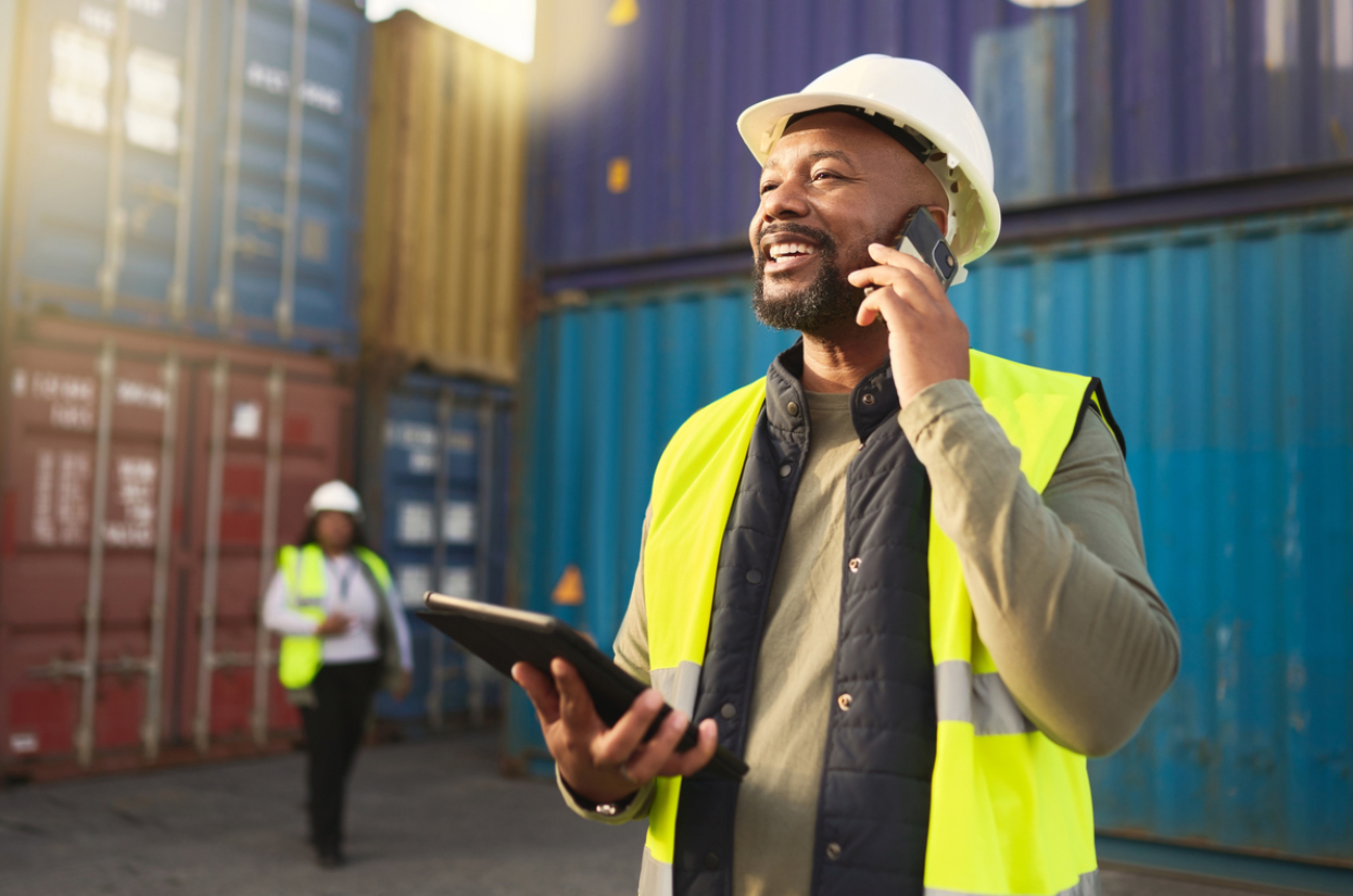 Logistics, shipping and construction worker on the phone with tablet in shipyard. Transportation engineer on smartphone in delivery, freight and international distribution business in container yard